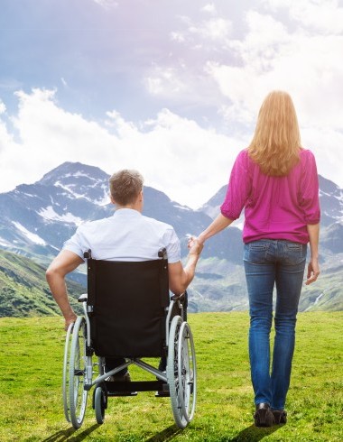 A man in a wheelchair and his female companion enjoy the magnificent mountain panorama.