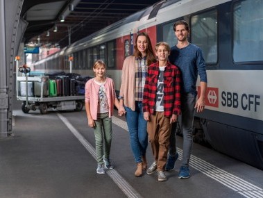 Familie und Gepäck stehen an einem Gleis an einem BHF