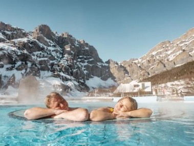 Ein Mann und eine Frau sitzen im Whirlpool, hinten sieht man die eindrückliche Bergkulisse